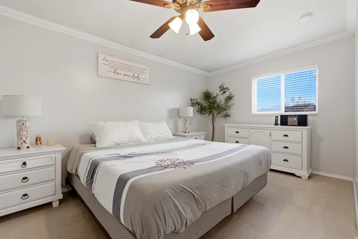 Bedroom with light colored carpet, ornamental molding, and a ceiling fan