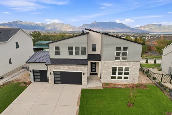 Contemporary exterior with stone and siding facade, black metal roof accents, and an attached two-car garage