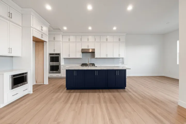 Two tone kitchen with stainless steel appliances, dual tone cabinets, light wood-style floors, light stone counters, and recessed lighting
