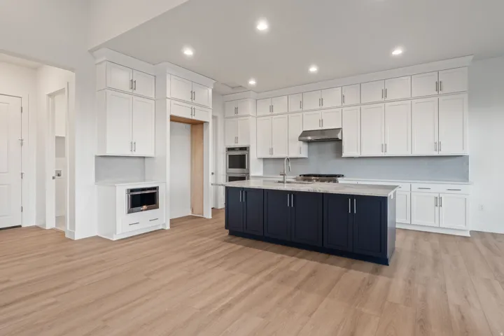 Dual tone kitchen with two tone cabinets, light wood-style flooring, recessed lighting, light stone counters, and a center island with sink