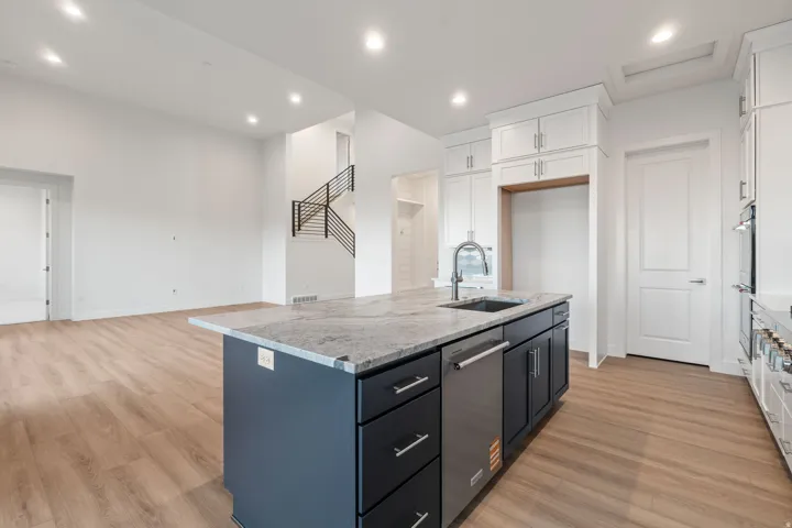 Kitchen with two tone cabinetry, light stone countertops, a center island with sink, light wood finished floors, and stainless steel appliances