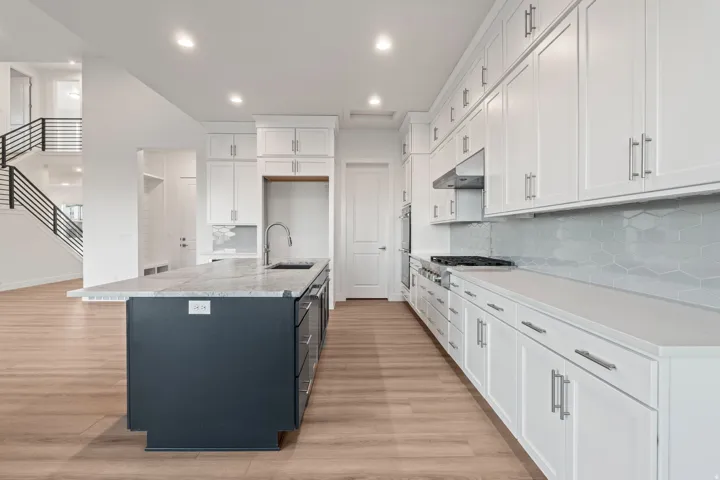 Kitchen with two tone cabinets, an island with sink, light wood finished floors, light stone counters, and tasteful backsplash