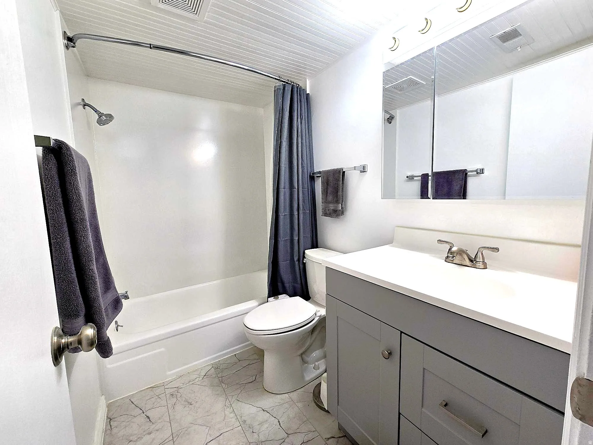Updated bathroom featuring vanity, shower / bath combo with shower curtain, and light marble finish floors