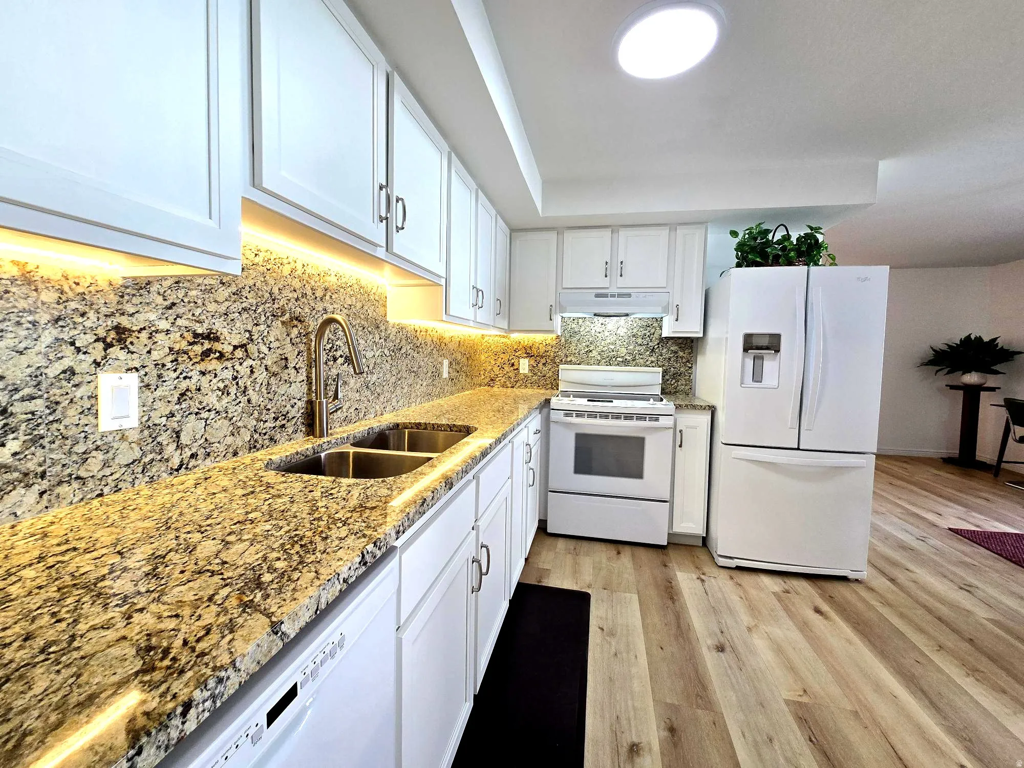 Kitchen with white appliances, white cabinetry, granite counters, under-cabinet lighting, and tasteful backsplash