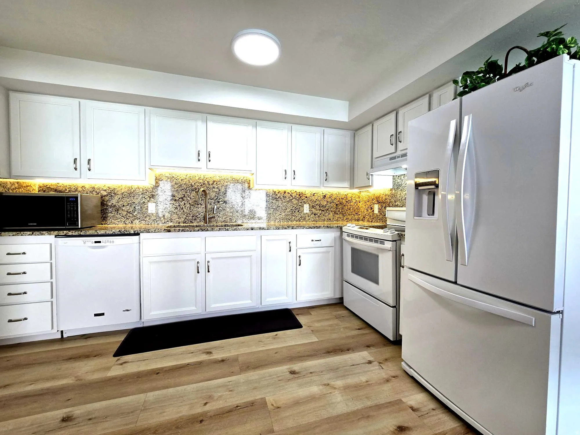 Kitchen with white appliances, white cabinetry, under cabinet lighting, granite counters, and tasteful backsplash