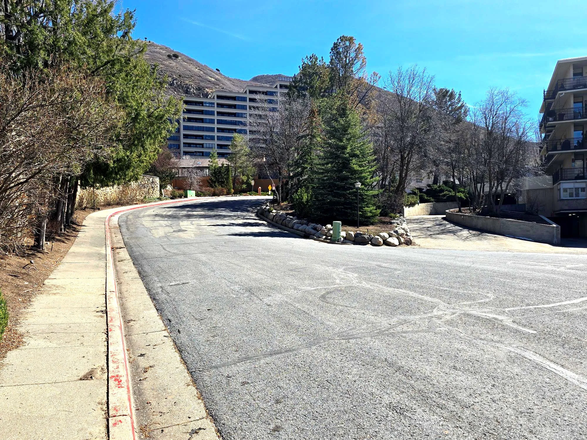 View of asphalt road with sidewalks, a mountain view, and curbs