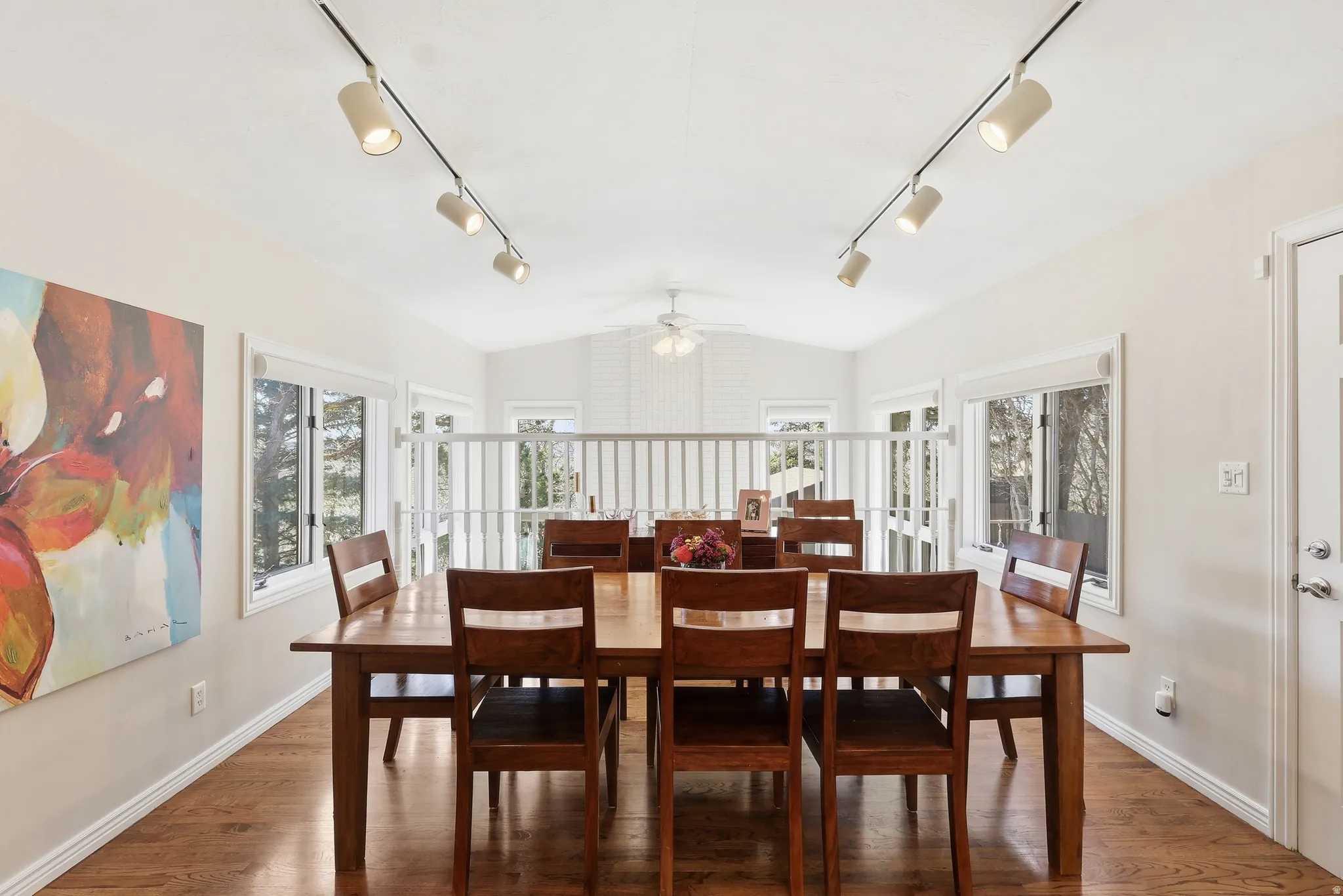 Dining space with ceiling fan, plenty of natural light, vaulted ceiling, wood finished floors, and rail lighting