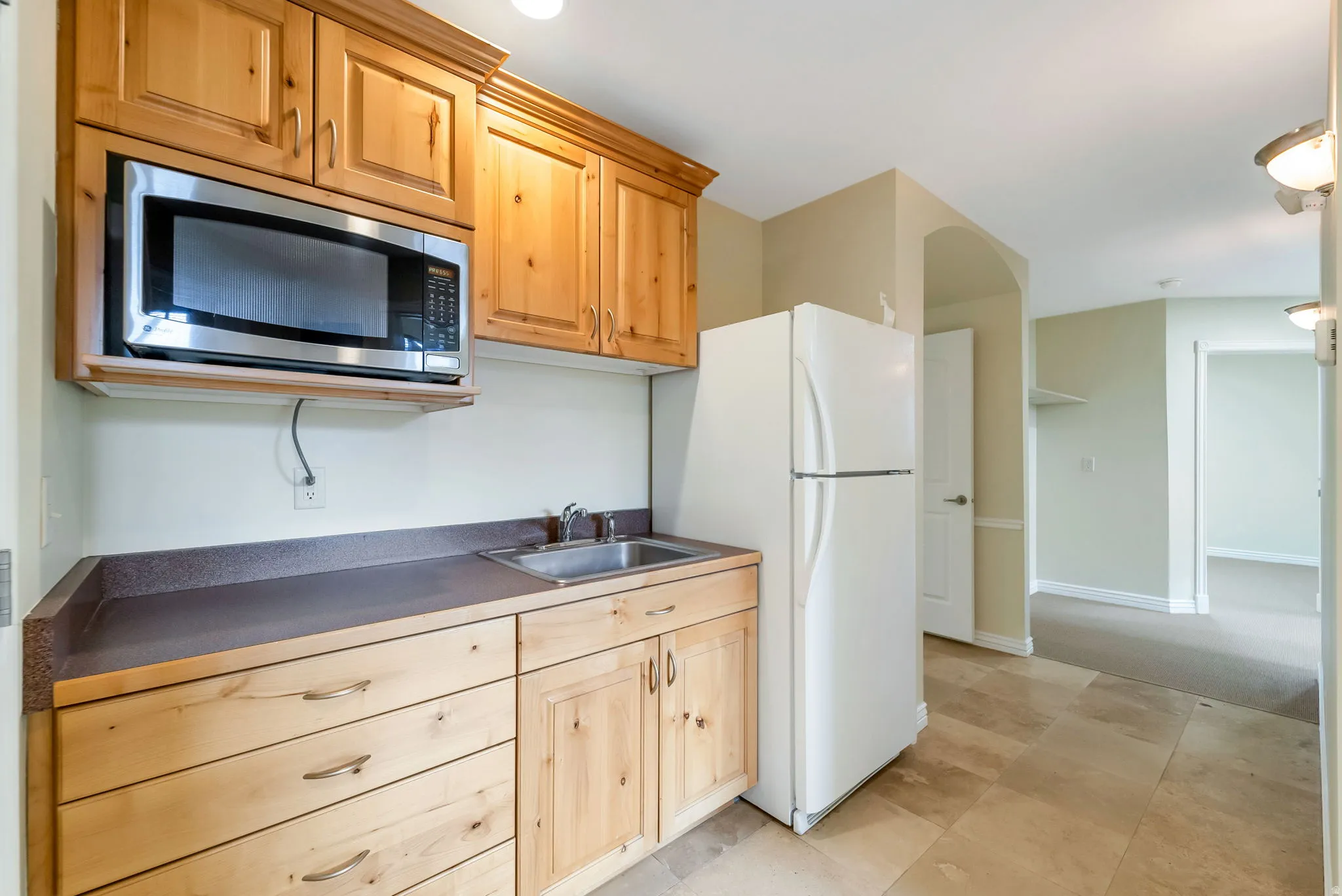 Kitchen featuring dark countertops, stainless steel microwave, freestanding refrigerator, and light wood finish cabinets