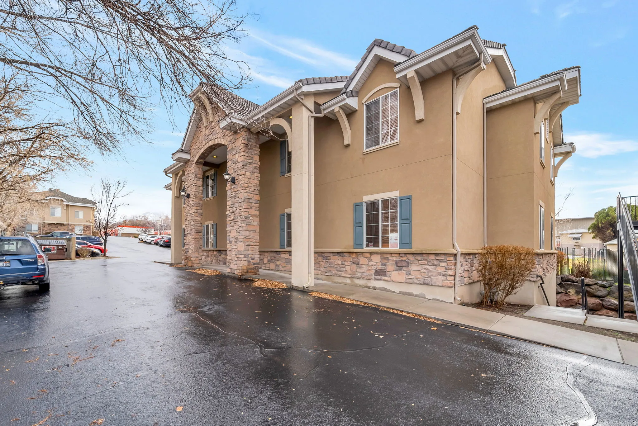 View of side of property with stucco siding, stone siding, a tiled roof, and uncovered parking