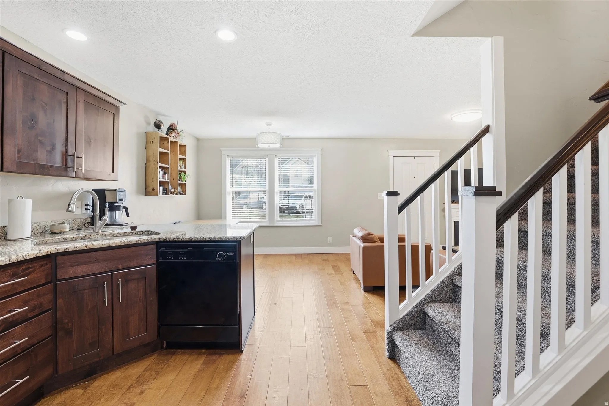 Kitchen with dark wood finish cabinets, dishwasher, light stone countertops, light wood finished floors, and a peninsula