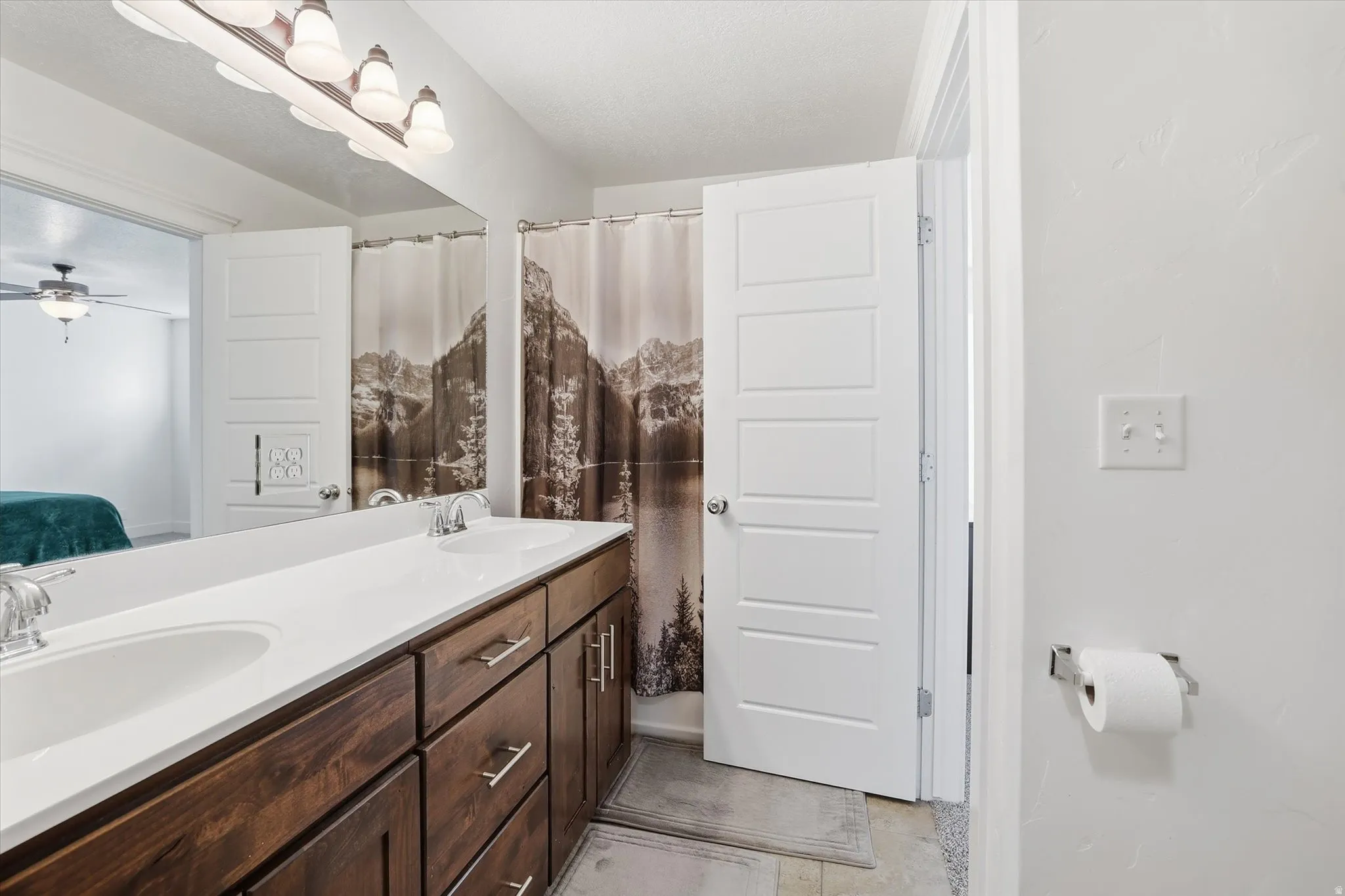 Ensuite bathroom featuring double vanity, a shower with curtain, and a ceiling fan