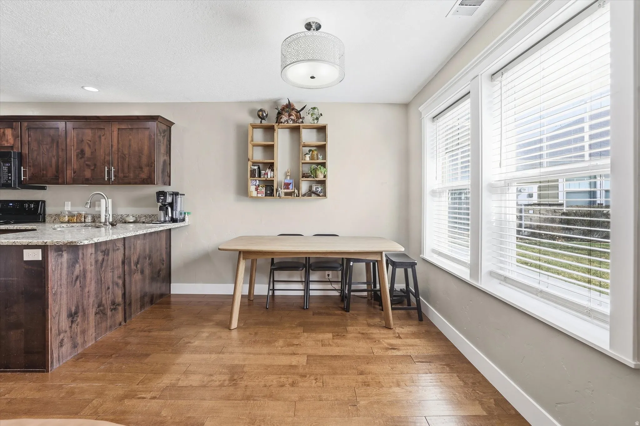 Kitchen with dark wood finish cabinets, light wood-style floors, light stone countertops, a peninsula, and black appliances