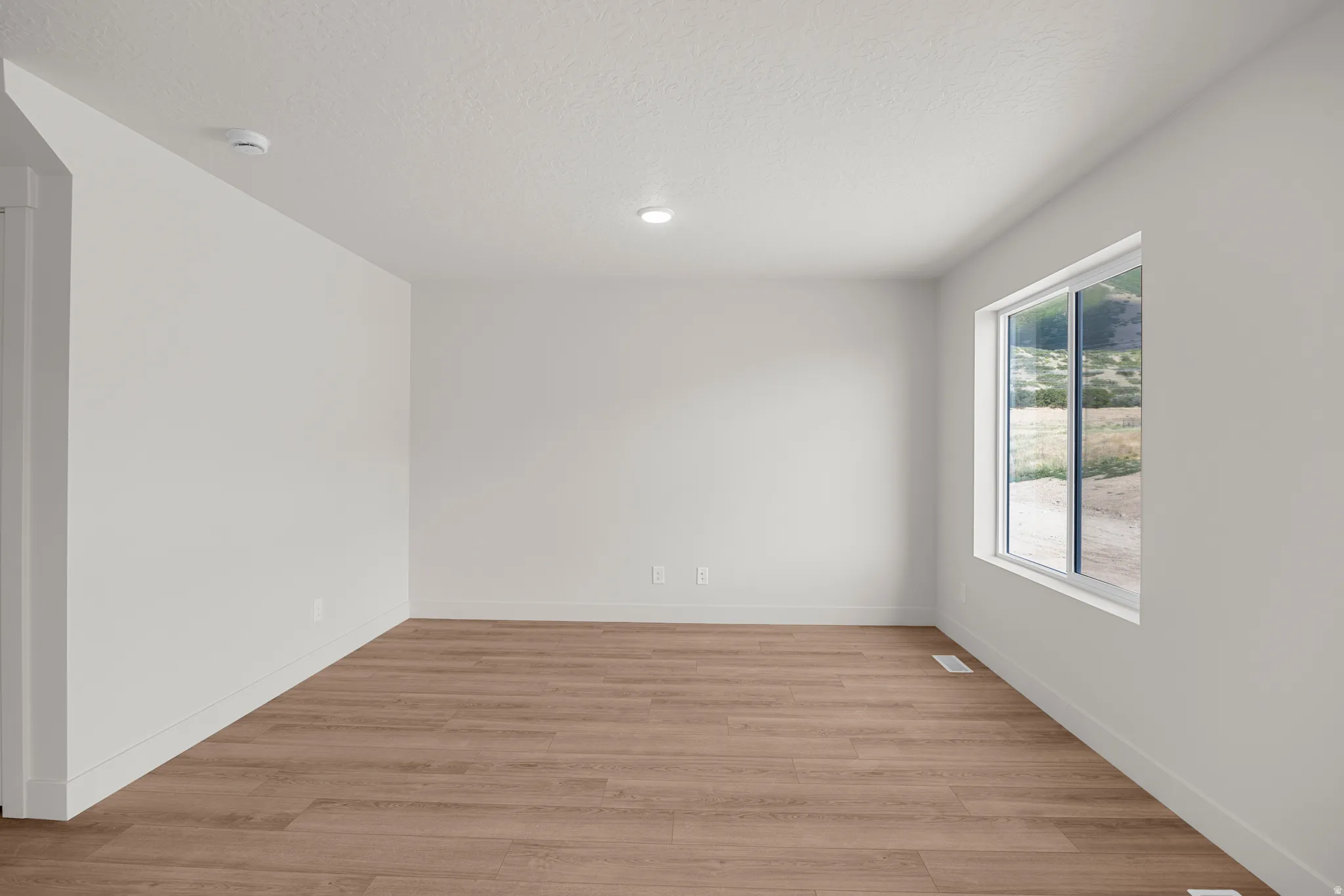 Empty room featuring light wood finished floors and a textured ceiling
