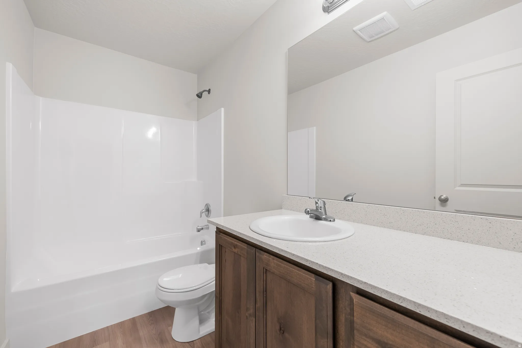 Bathroom featuring vanity, light wood-type flooring, shower / bathtub combination, and a textured ceiling