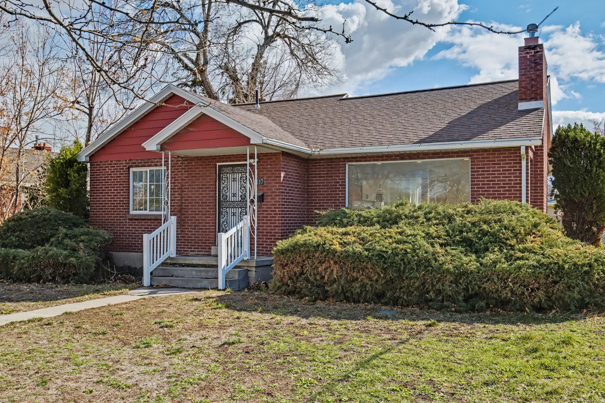 View of front of house with a chimney, brick siding, roof with shingles, and a front yard