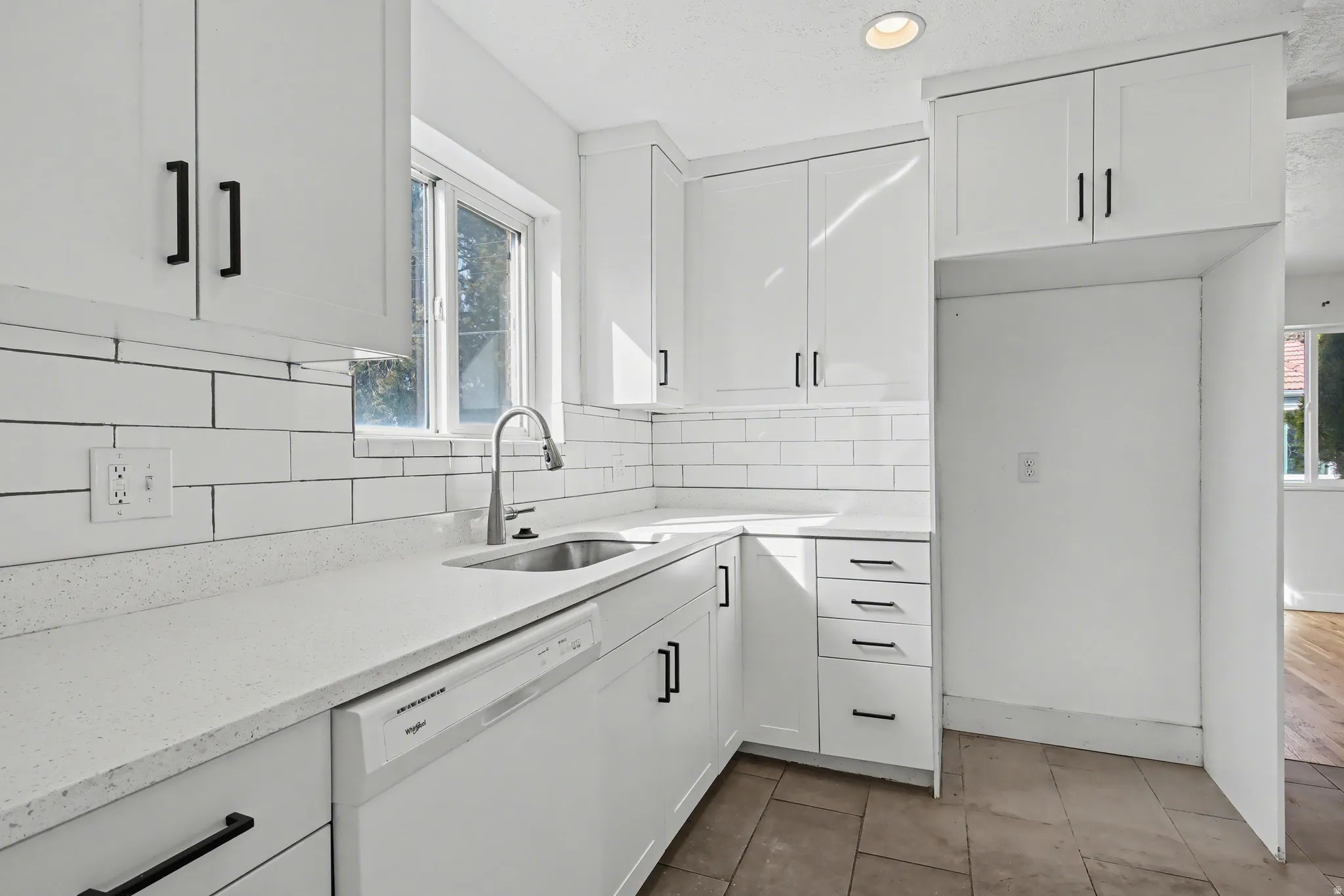 Kitchen featuring dishwasher, backsplash, white cabinets, light stone counters, and plenty of natural light