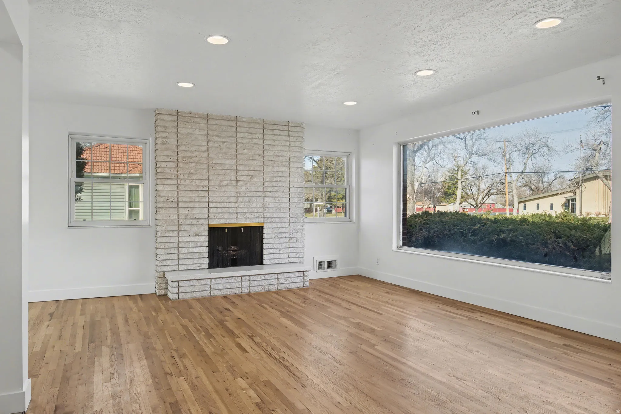 Unfurnished living room with a fireplace, light wood-style flooring, recessed lighting, plenty of natural light, and a textured ceiling