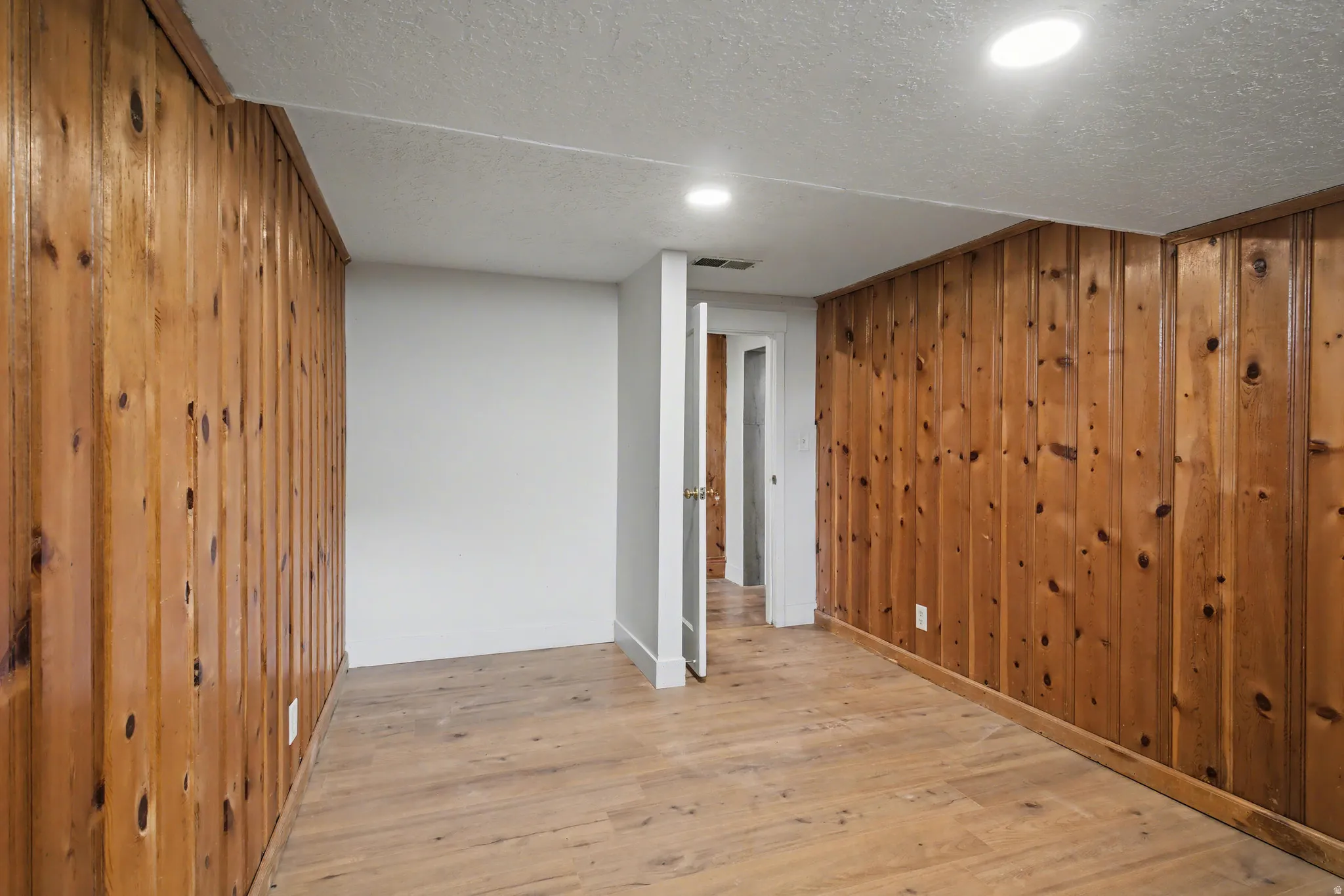 Spare room with wood walls, light wood finished floors, a textured ceiling, and recessed lighting