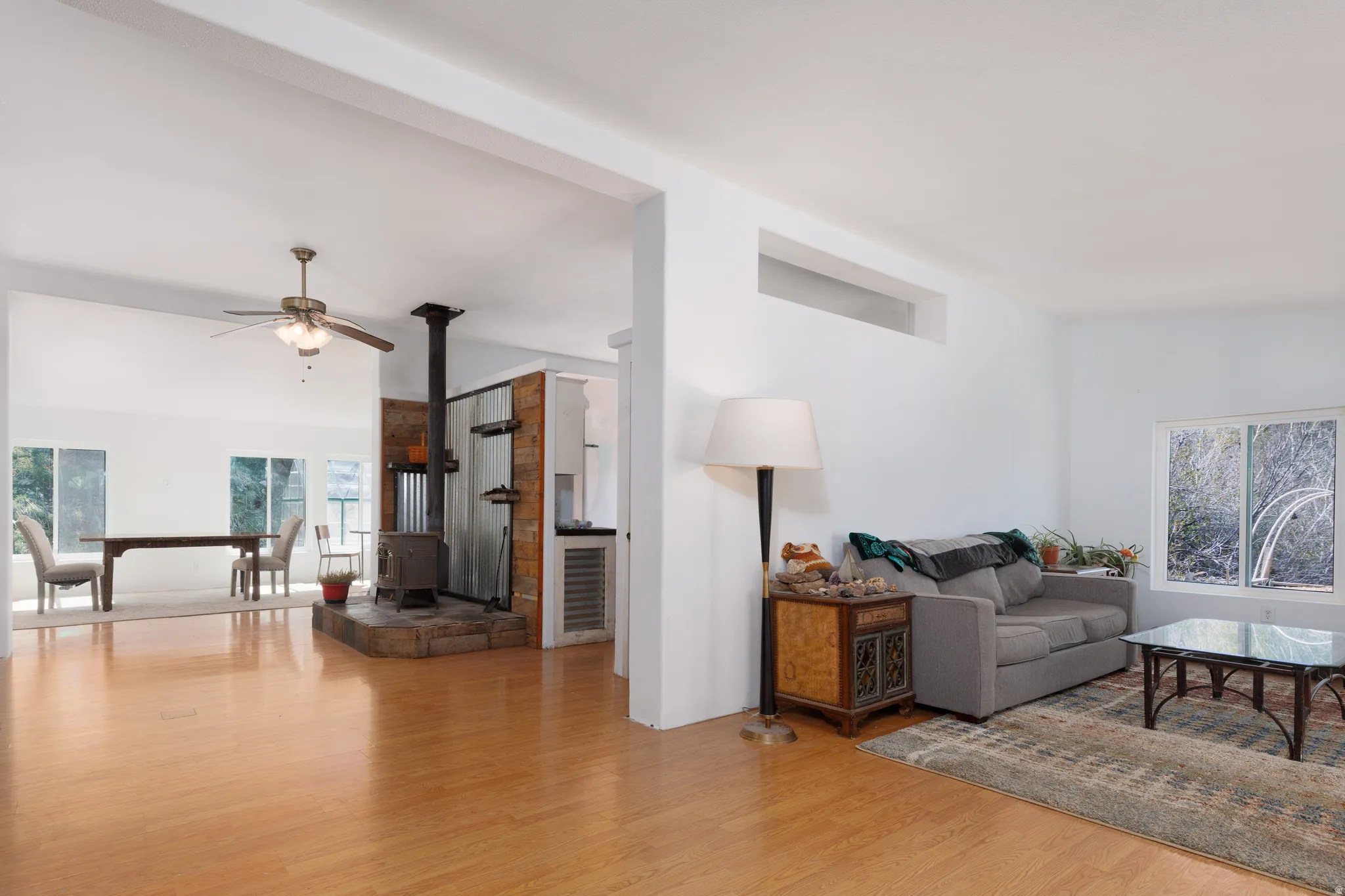 Living area featuring a wood stove, light wood-style floors, ceiling fan, and healthy amount of natural light