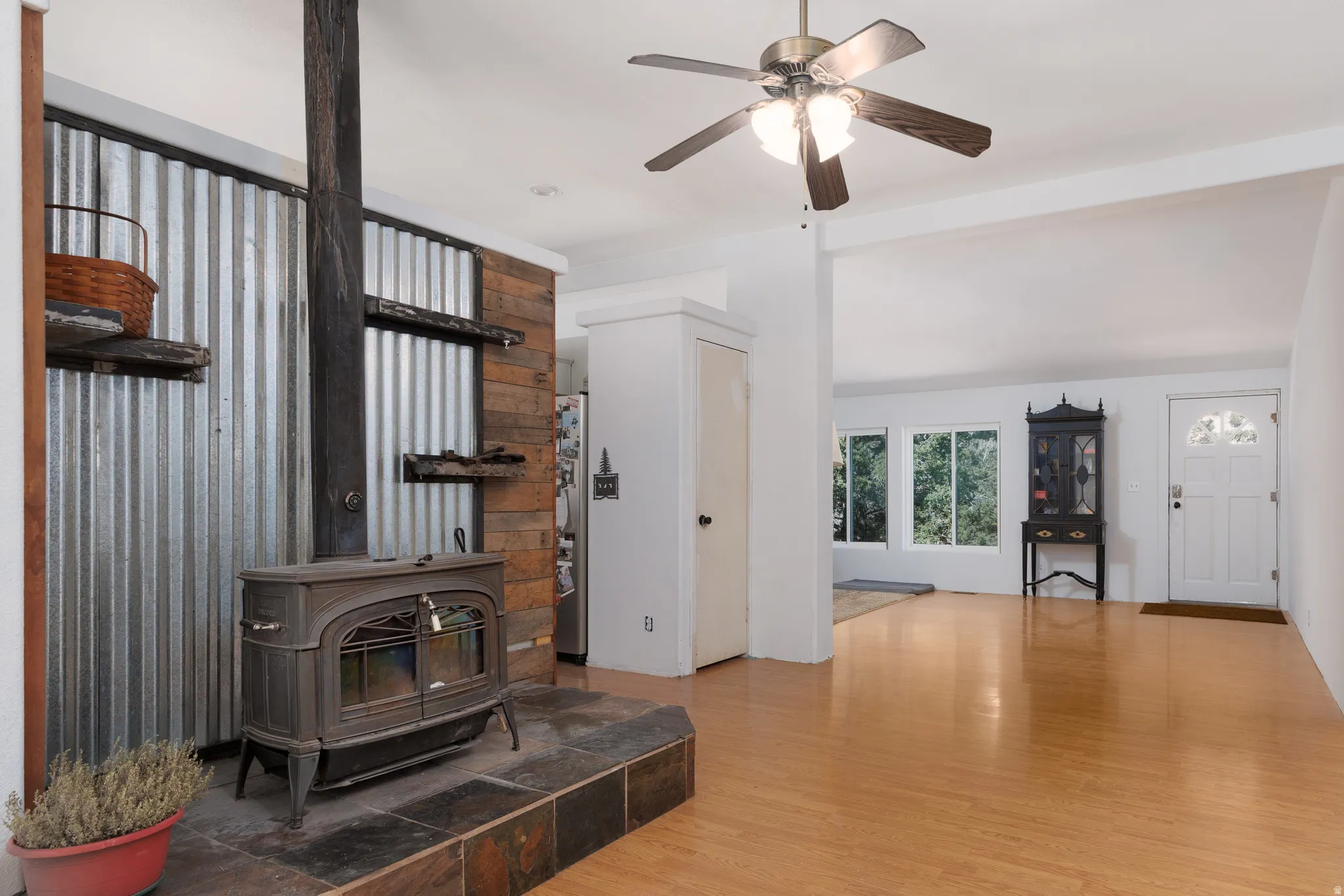 Living area featuring ight wood-style floors, ceiling fan, and a wood stove