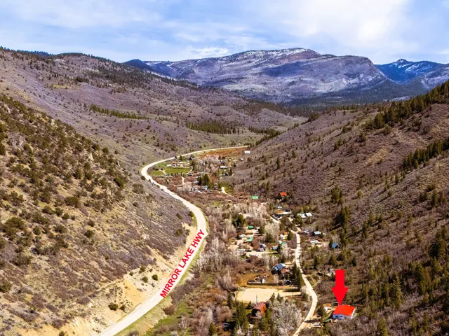 Mountain valley property featuring a red-roofed structure nestled among trees, with a winding roadway nearby