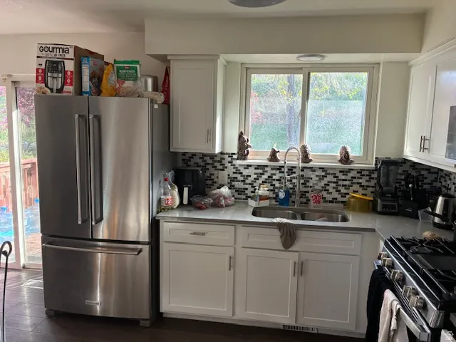 Kitchen featuring stainless steel appliances, white cabinetry, light stone counters, and decorative backsplash