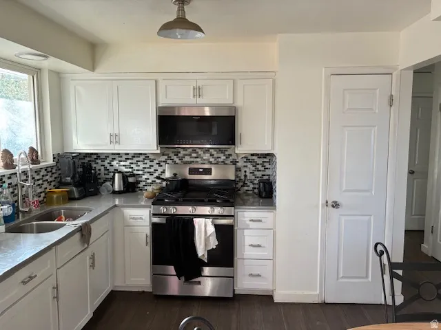 Kitchen with stainless steel appliances, white cabinetry, dark wood-style floors, and light stone countertops