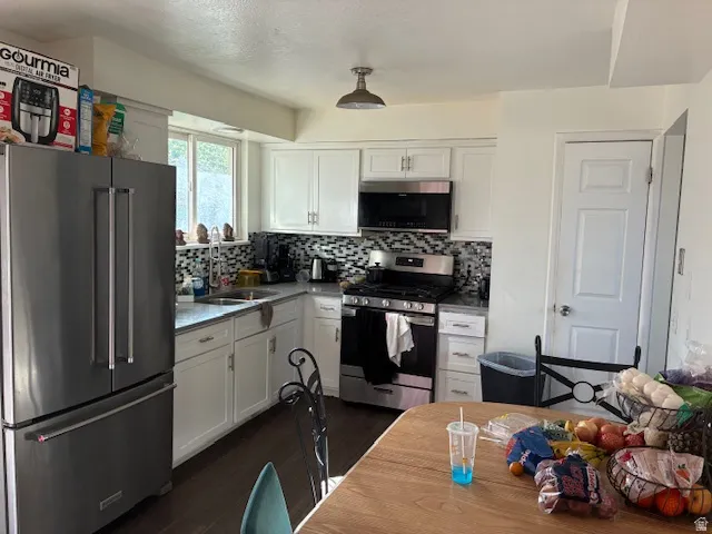 Kitchen featuring stainless steel appliances, white cabinets, backsplash, dark wood-style flooring, and a textured ceiling