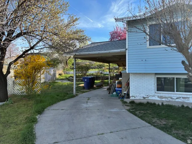 View of home's exterior featuring brick siding, driveway, a yard, a carport, and roof with shingles