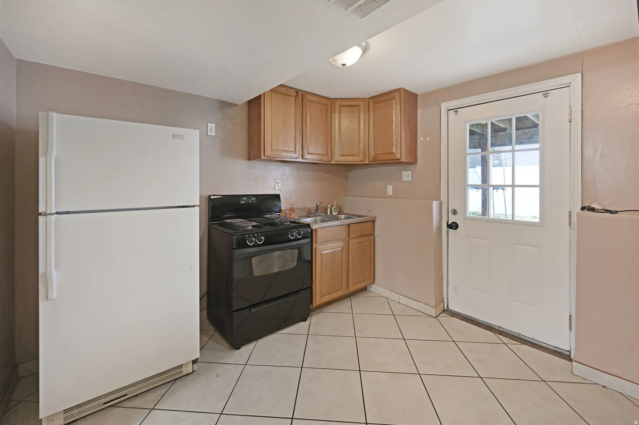 Kitchen featuring freestanding refrigerator, black range with gas cooktop, light countertops, and light tile patterned floors