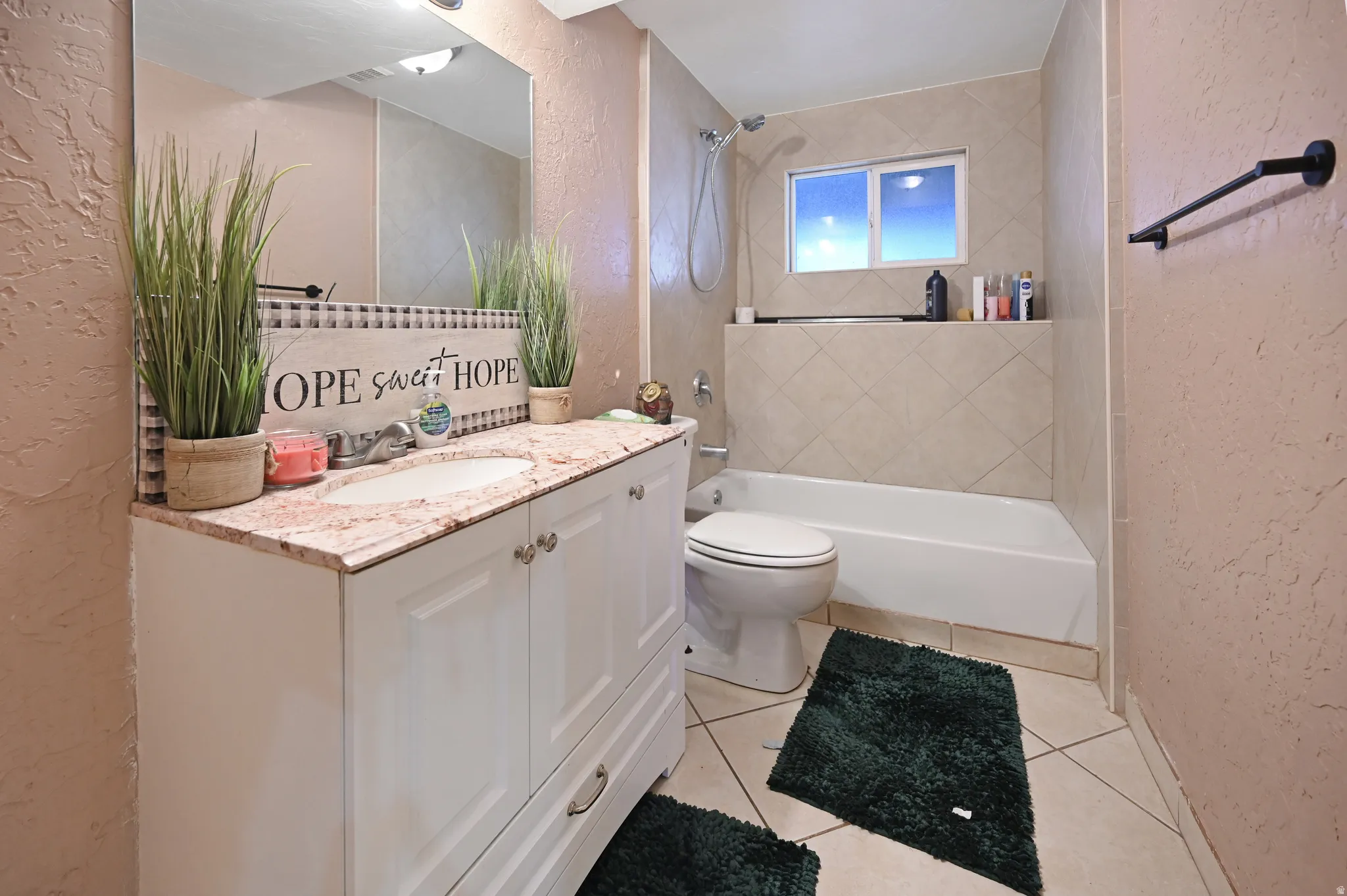 Bathroom with a textured wall, vanity, bathtub / shower combination, light tile patterned flooring, and backsplash