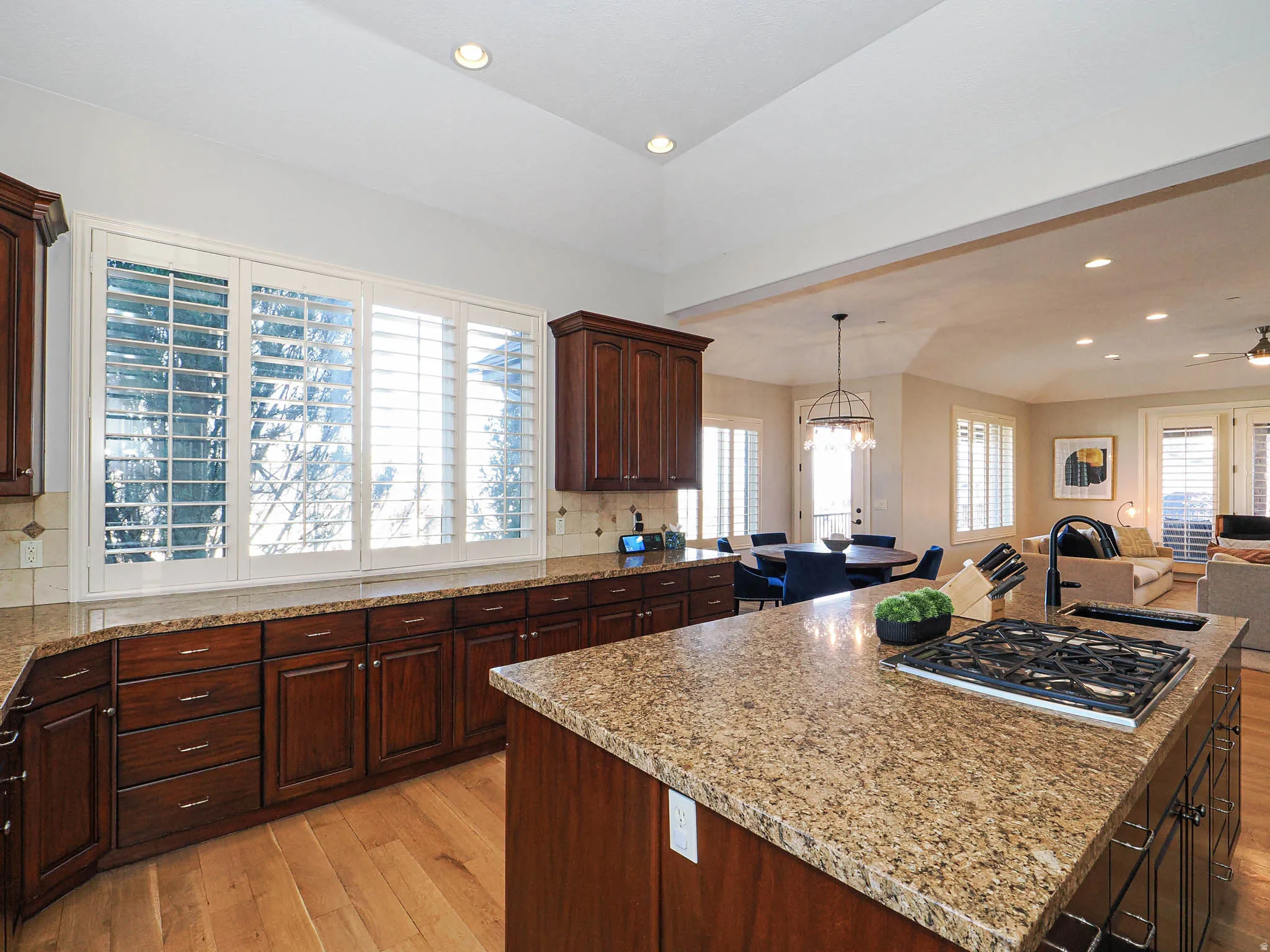 Kitchen with open floor plan, light wood finished floors, dark wood finish cabinets, backsplash, and a center island with sink