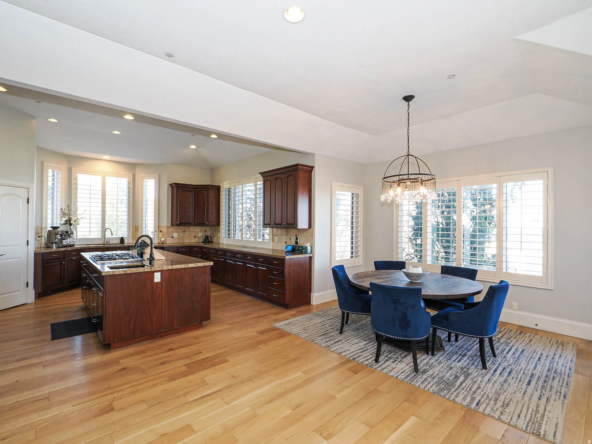 Kitchen with an island with sink, light wood finished floors, light stone countertops, dark wood finish cabinetry, and vaulted ceiling
