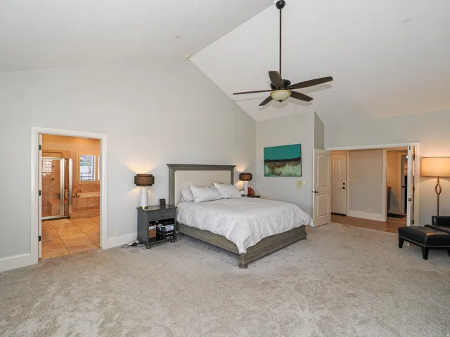 Bedroom with light colored carpet, ensuite bathroom, ceiling fan, and a high ceiling