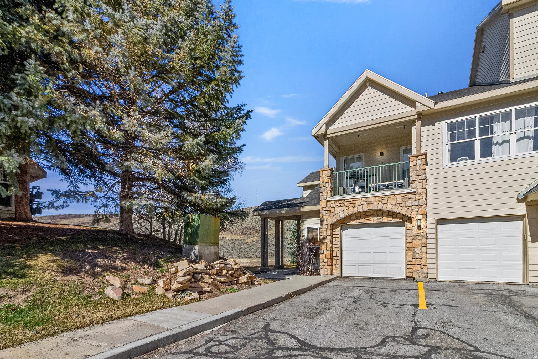 View of front of home featuring a balcony, asphalt driveway, an attached garage, and stone siding