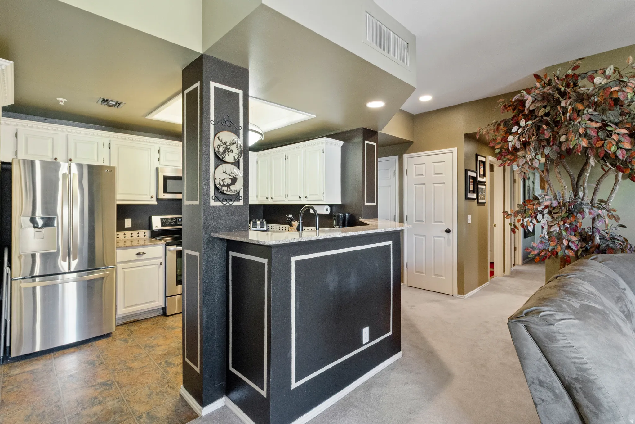 Kitchen featuring stainless steel appliances, white cabinetry, light stone counters, recessed lighting, and dark carpet