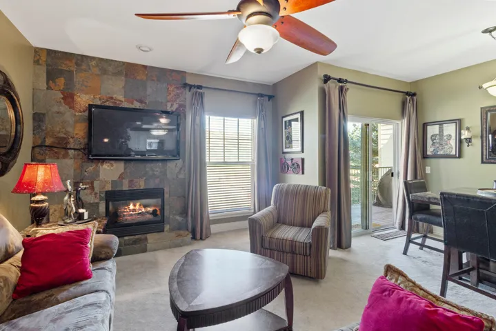 Living area with a tile fireplace, light carpet, and ceiling fan