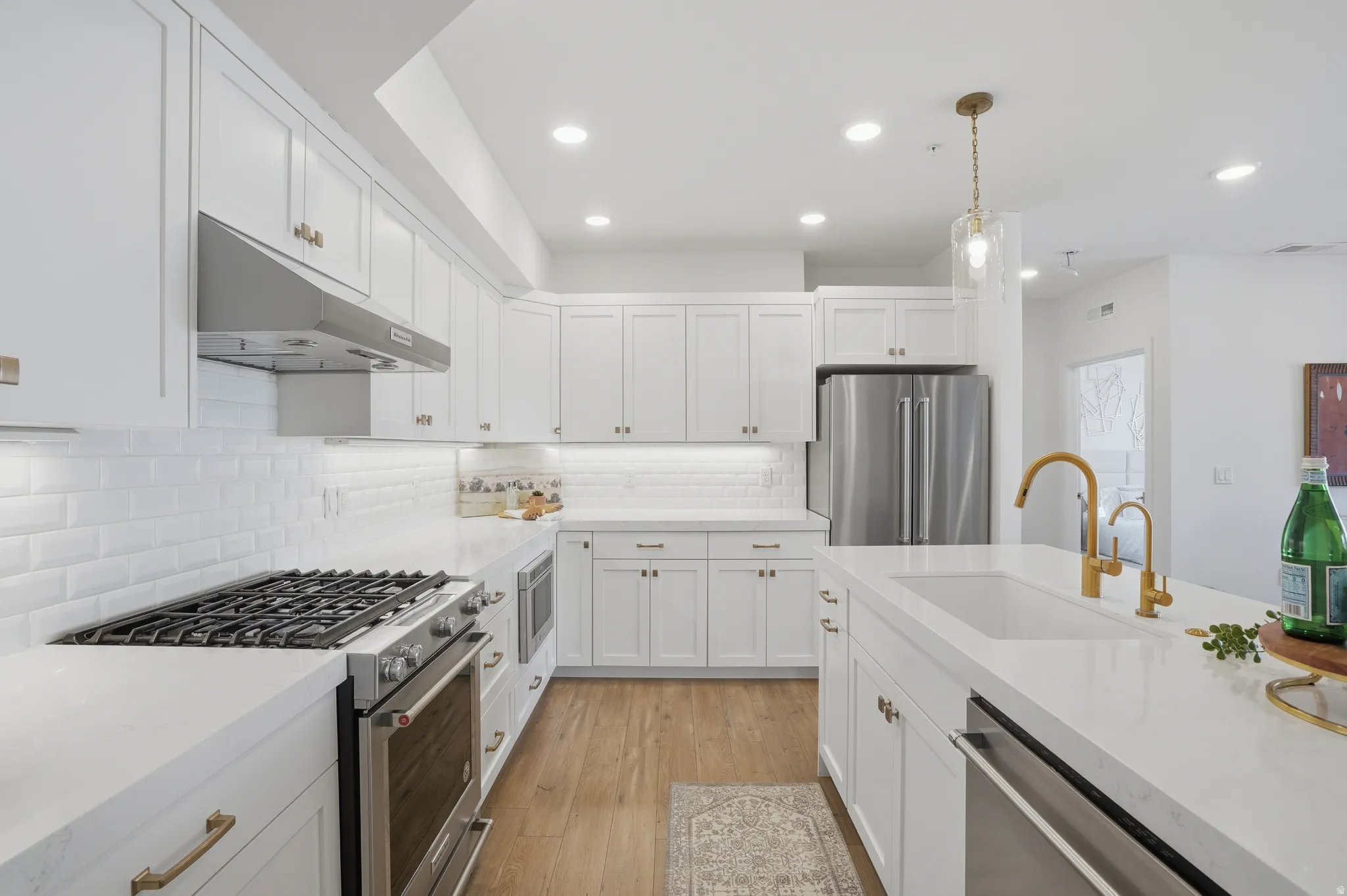 Kitchen featuring stainless steel appliances, pendant lighting, white cabinetry, light wood-type flooring, and light stone countertops