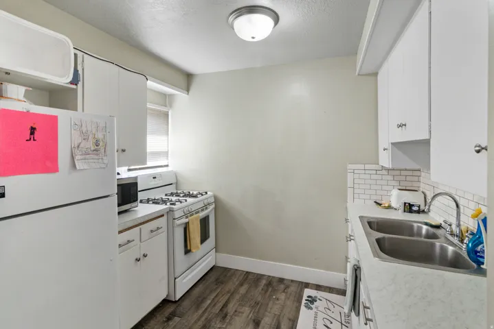 Kitchen with white cabinetry, white appliances, light countertops, a textured ceiling, and dark wood-type flooring