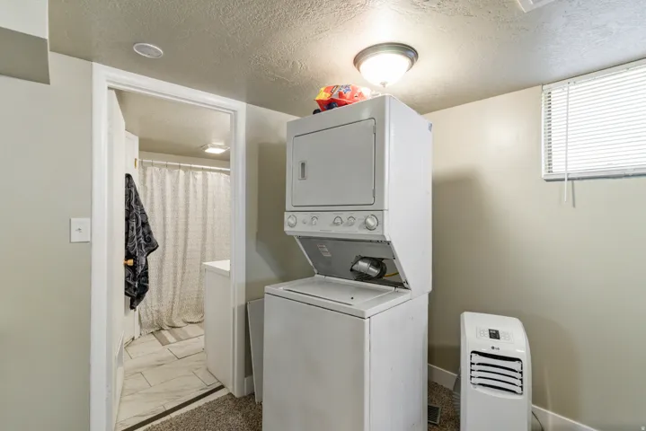 Laundry area featuring stacked washing machine and dryer, a textured ceiling, and light marble finish flooring
