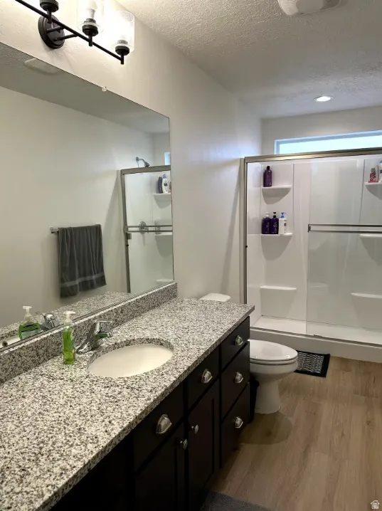Full bath featuring vanity, a textured ceiling, light wood finished floors, and a shower stall