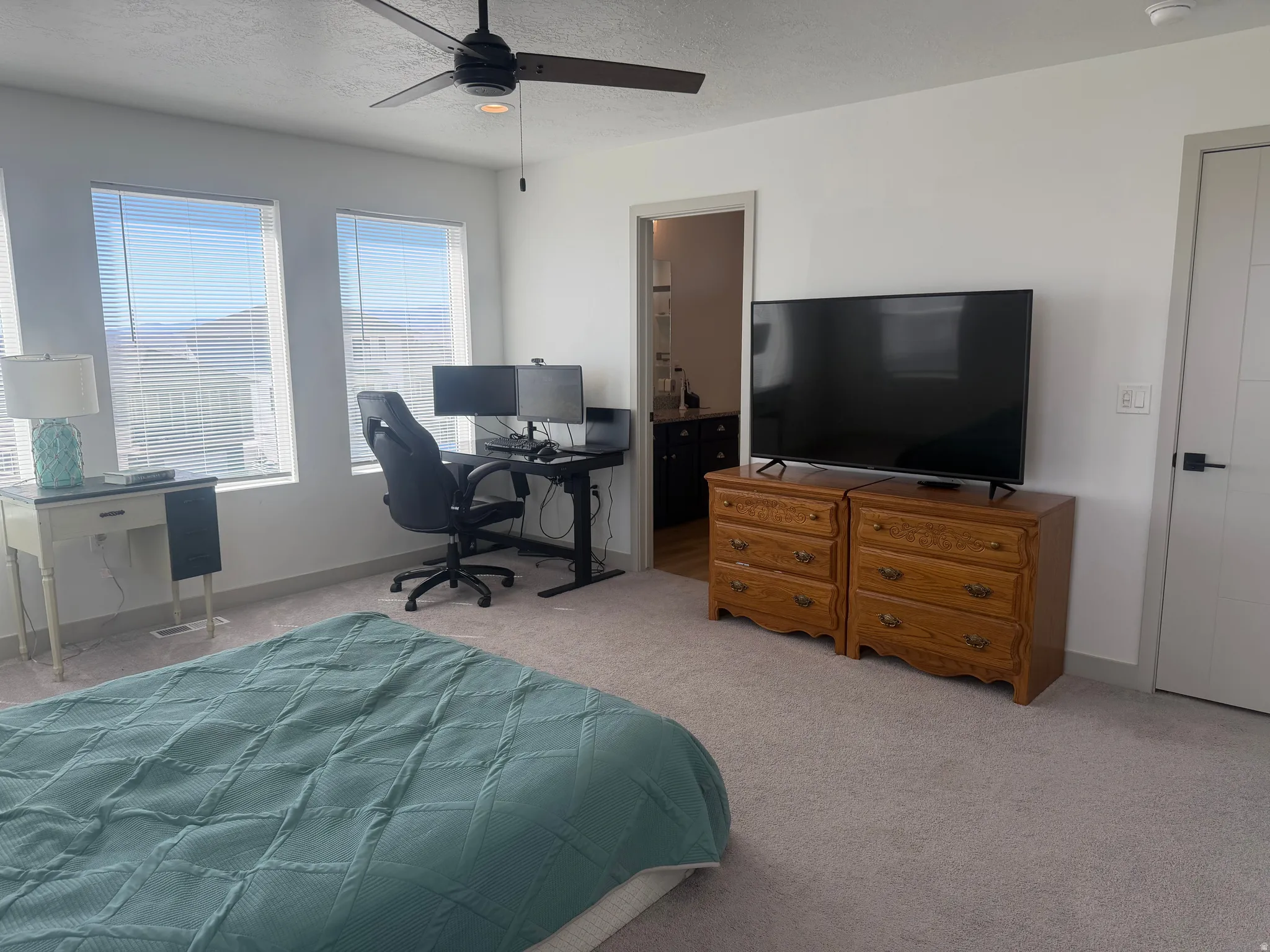 Bedroom with a desk, light colored carpet, a ceiling fan, connected bathroom, and a textured ceiling