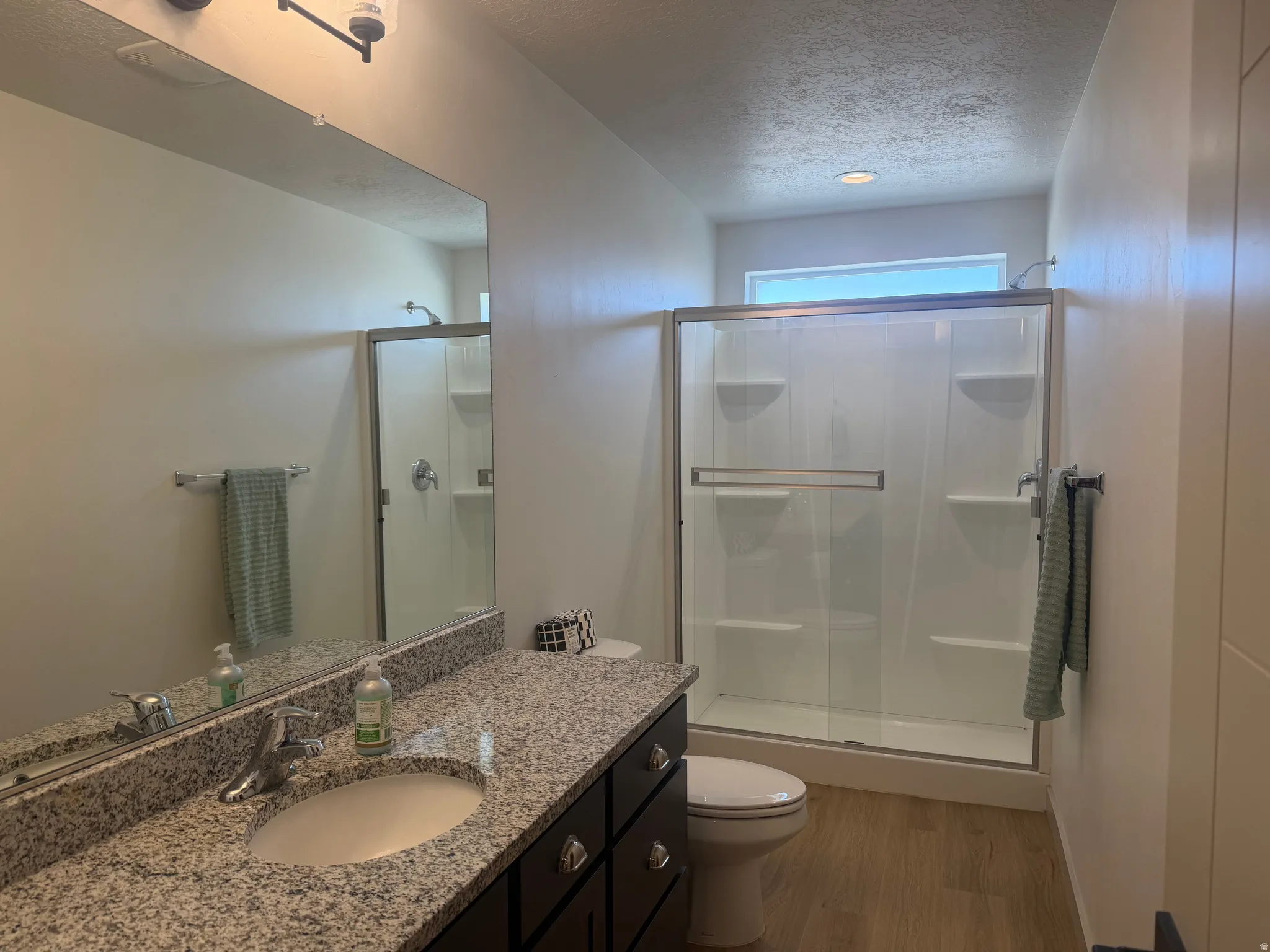 Full bath with vanity, a shower stall, a textured ceiling, and light wood-type flooring