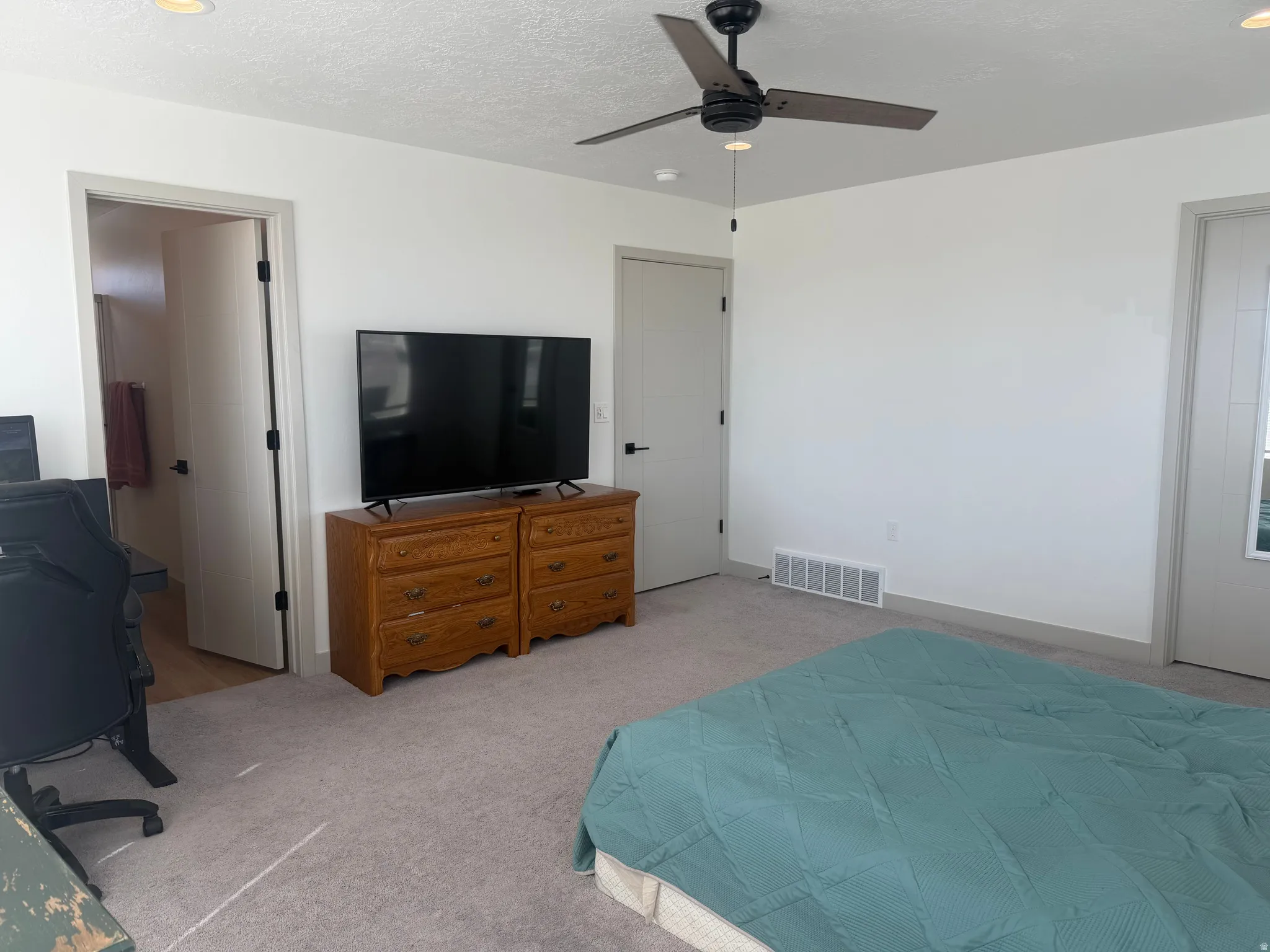 Bedroom with ceiling fan, light colored carpet, and a textured ceiling