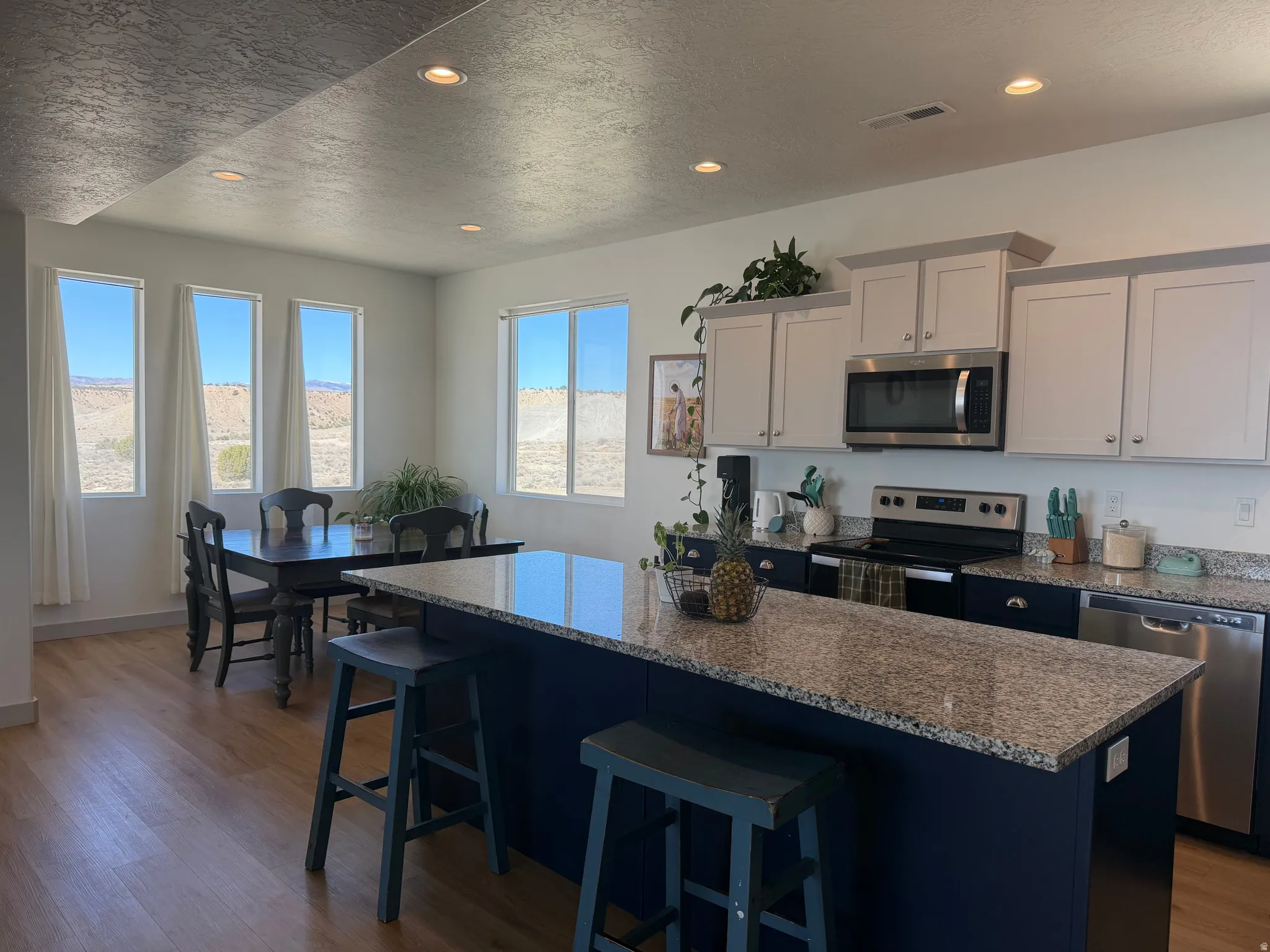 Dual tone kitchen with a kitchen breakfast bar, stainless steel appliances, light wood-type flooring, dark stone countertops, and a textured ceiling