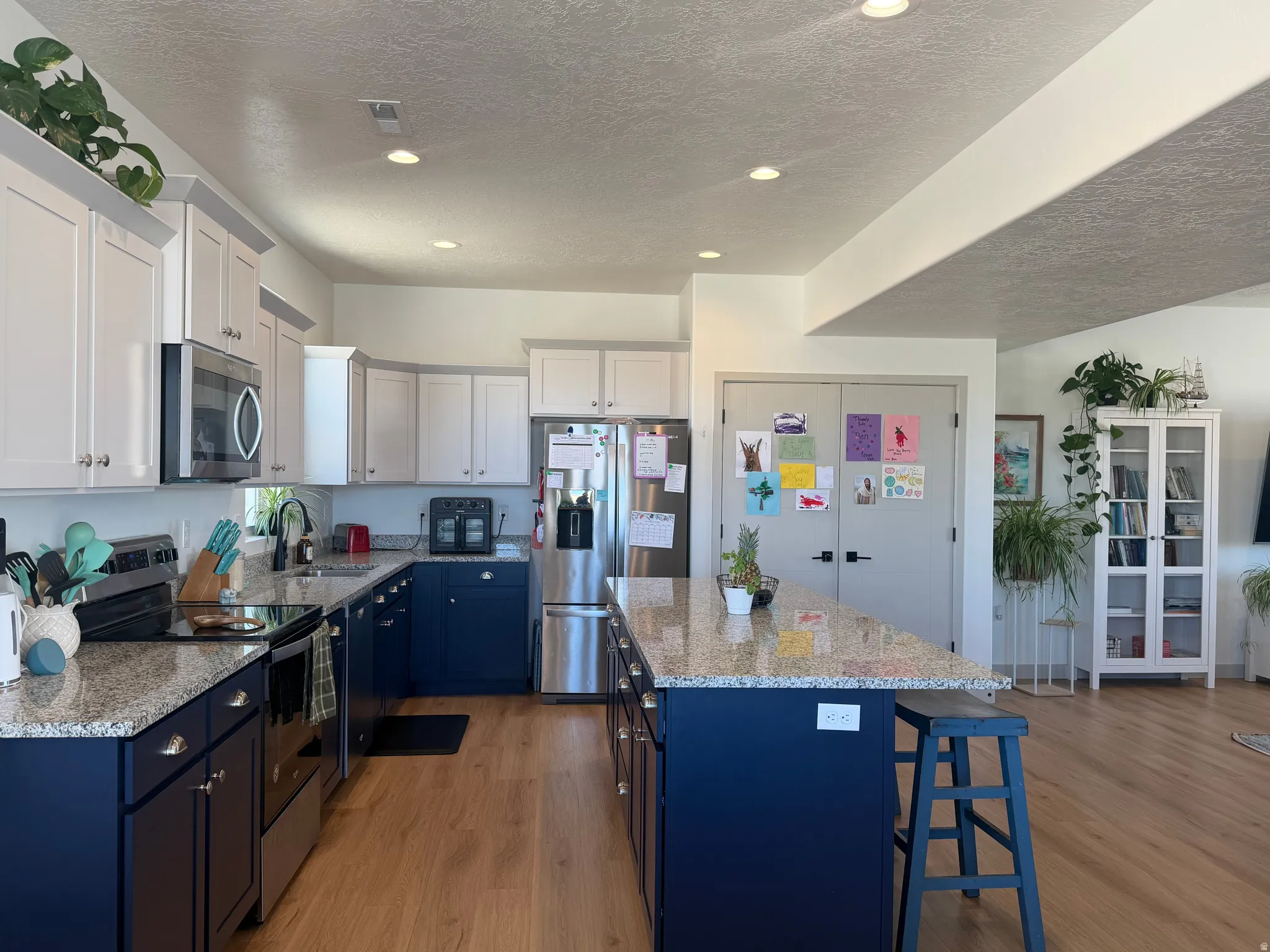 Dual tone kitchen featuring dual tone cabinetry, stainless steel appliances, light wood-type flooring, light stone counters, and a center island