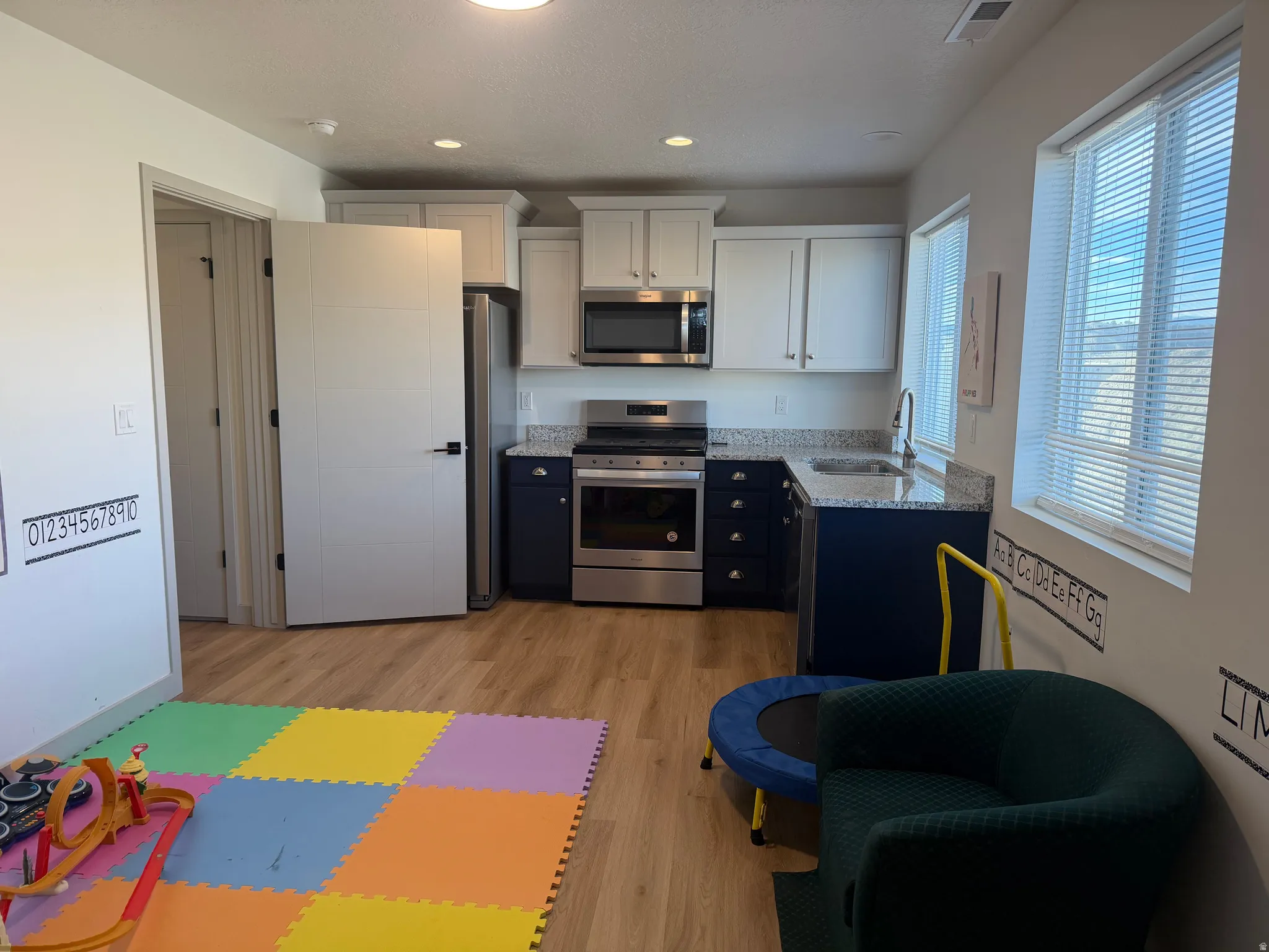 Dual tone kitchen featuring two tone color scheme, stainless steel appliances, light stone countertops, light wood finished floors, and recessed lighting