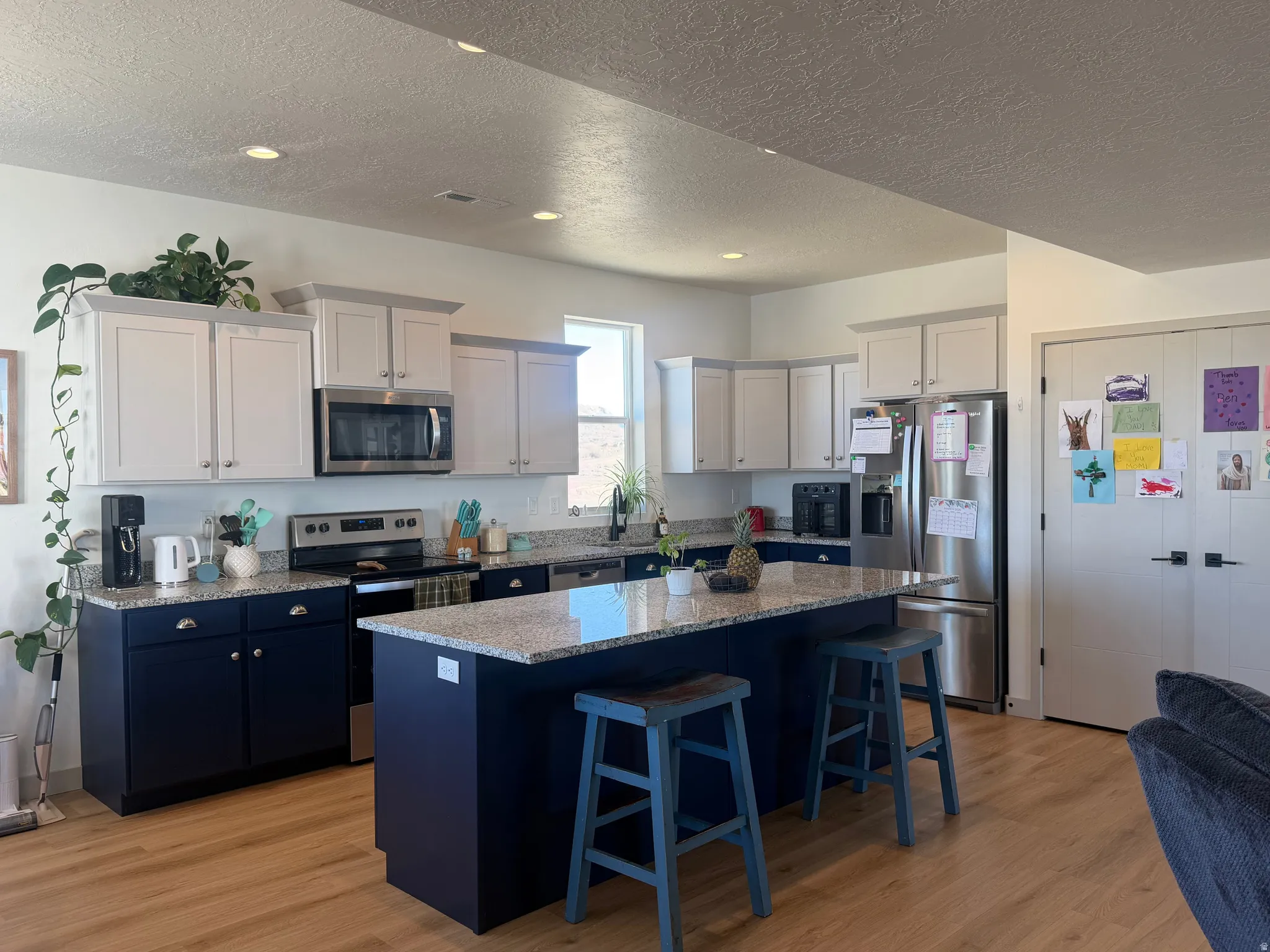 Two tone kitchen featuring stainless steel appliances, a center island, a kitchen breakfast bar, light stone countertops, and light wood-style flooring
