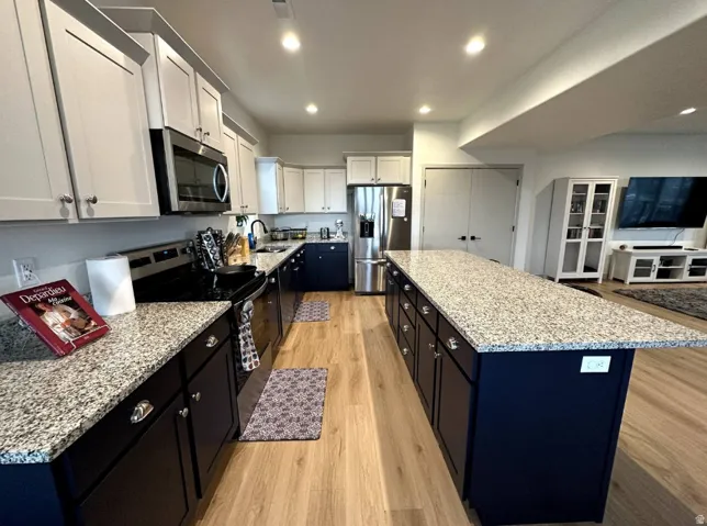 Two tone kitchen with stainless steel appliances, two tone color scheme, light stone counters, light wood finished floors, and a kitchen island