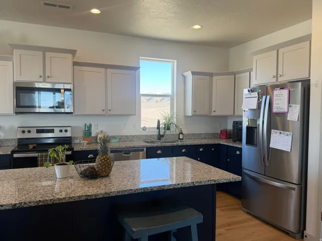 Kitchen with stainless steel appliances, a textured ceiling, light wood-type flooring, light stone countertops, and a kitchen breakfast bar